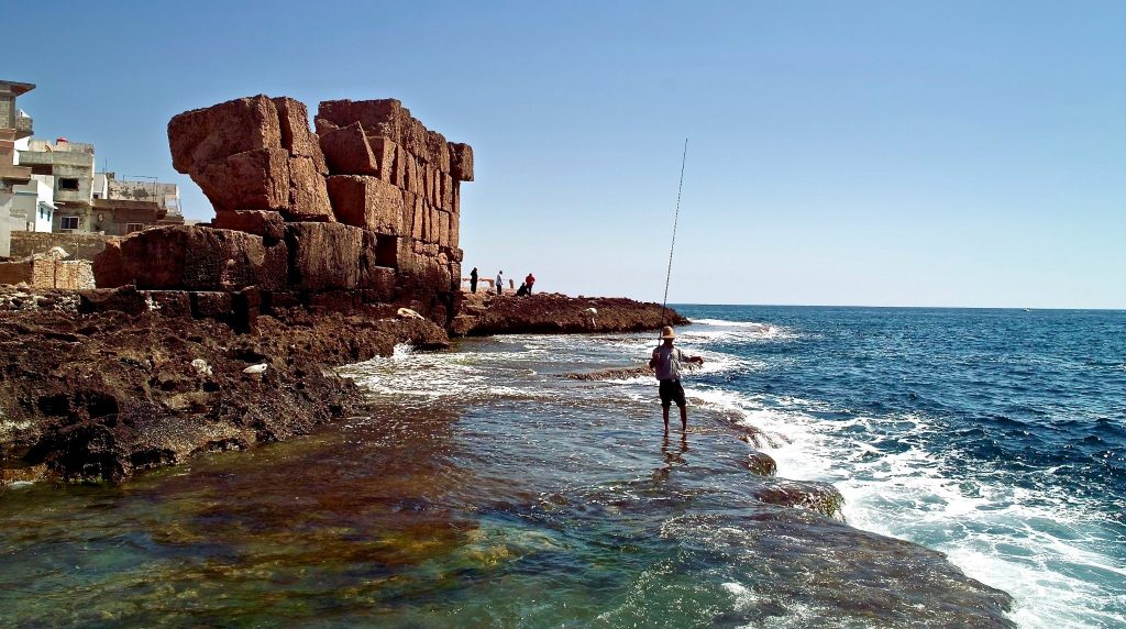 Un pêcheur au bord de la mer, près de vestiges en pierre sur l’île d’Arwad, en Syrie.