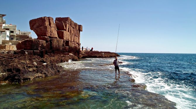 Un pêcheur au bord de la mer, près de vestiges en pierre sur l’île d’Arwad, en Syrie.